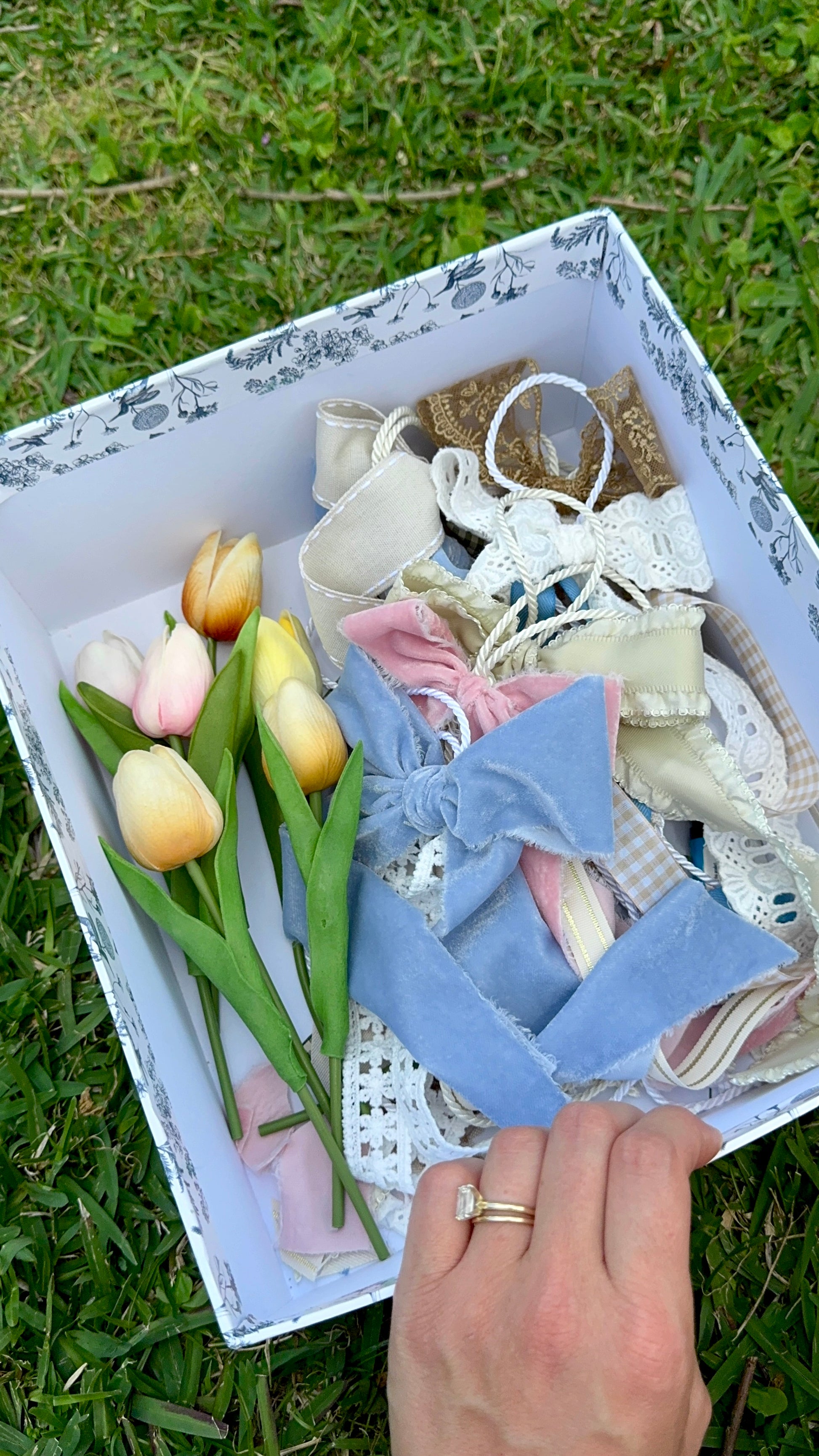 Box with decorative items including ribbons and tulips on a grassy background